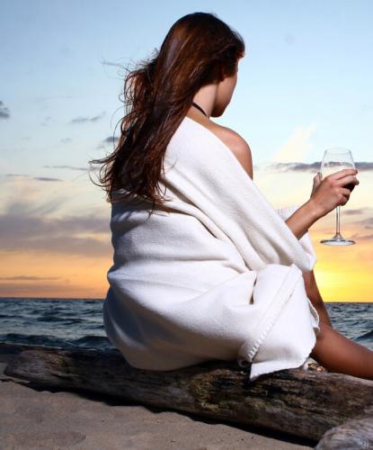 Donna sulla spiaggia al tramonto con bicchiere di vino.