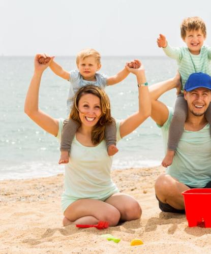 Famiglia felice gioca sulla spiaggia con secchiello e paletta.