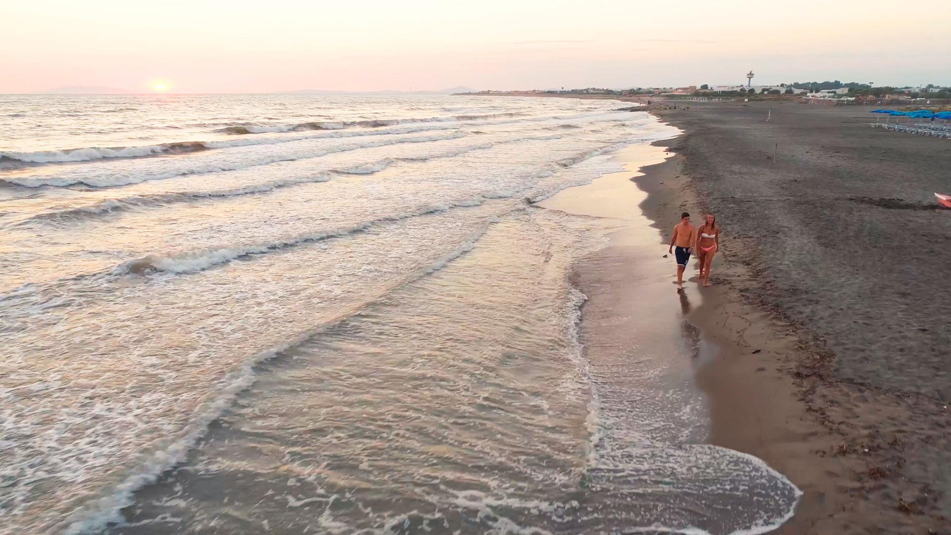 Coppia cammina sulla spiaggia al tramonto, onde leggere e cielo sereno.