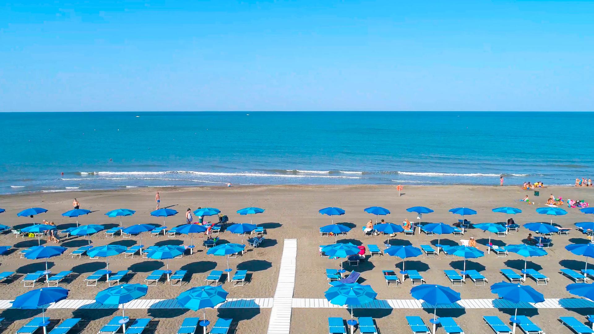 Spiaggia con ombrelloni blu, sdraio e mare calmo sotto un cielo sereno.