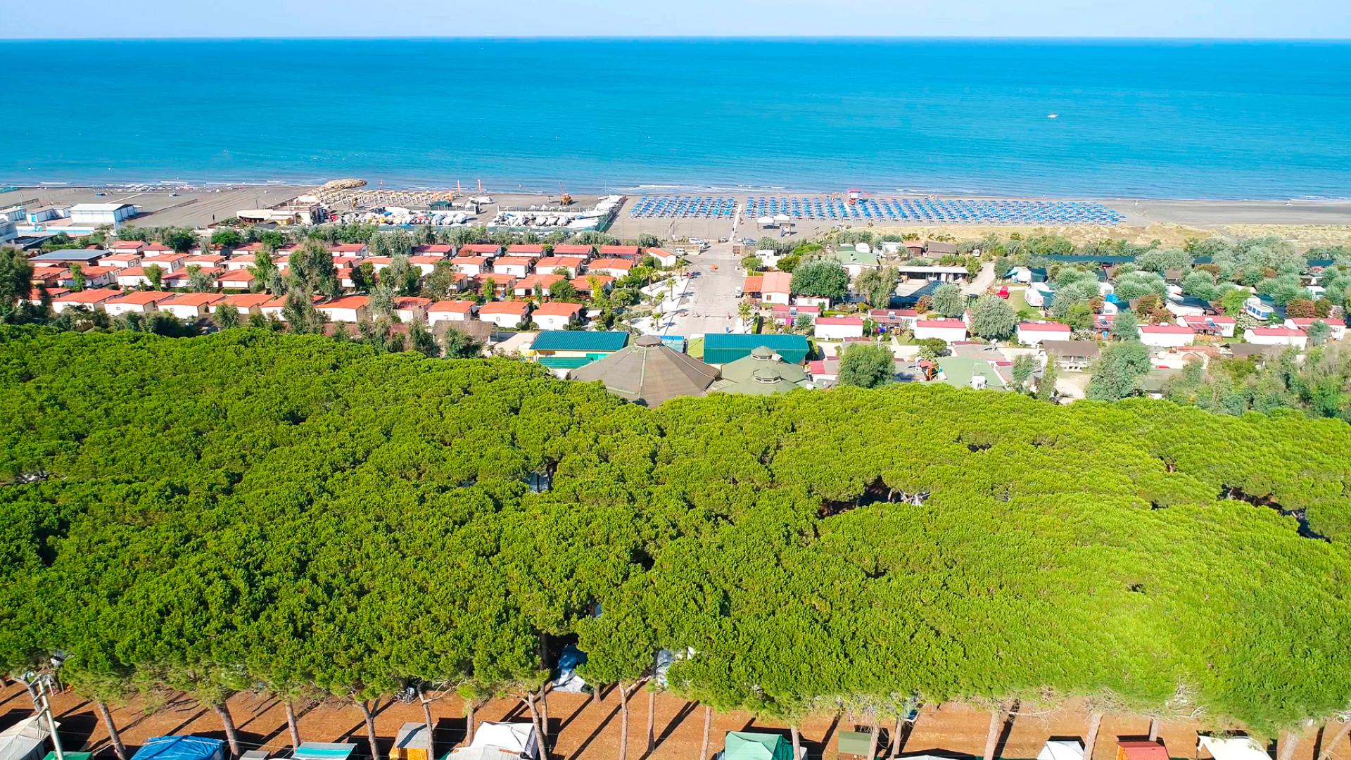 Vista aerea di un villaggio turistico con spiaggia e mare azzurro sullo sfondo.