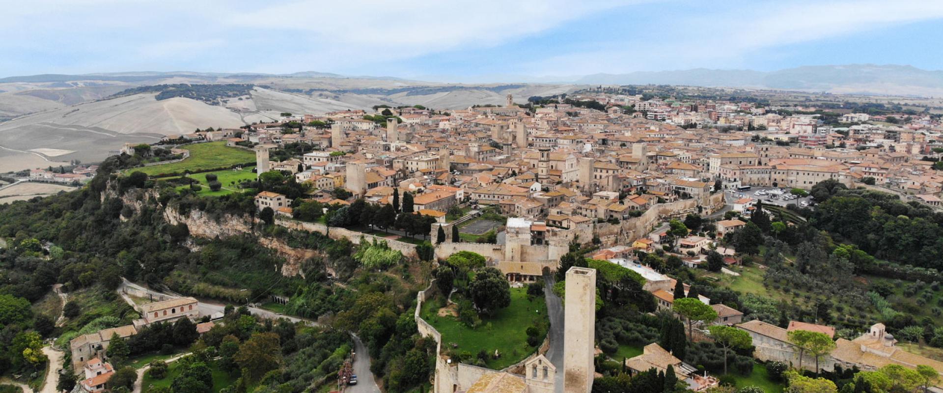 Panorama di un borgo medievale con torri, mura e paesaggio collinare.