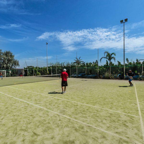 Partita di tennis su campo all'aperto con cielo sereno e palme sullo sfondo.