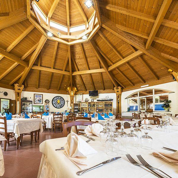 Ristorante accogliente con tetto in legno, tavoli apparecchiati elegantemente e atmosfera luminosa.