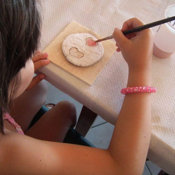 Bambina dipinge un cuore su un disco di argilla con un pennello.