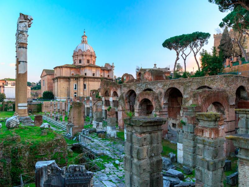 Rovine romane con colonne e cupola, circondate da pini e architettura antica.