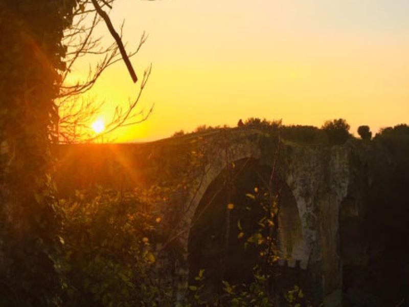 Tramonto su un antico ponte immerso nella natura, avvolto da colori caldi.